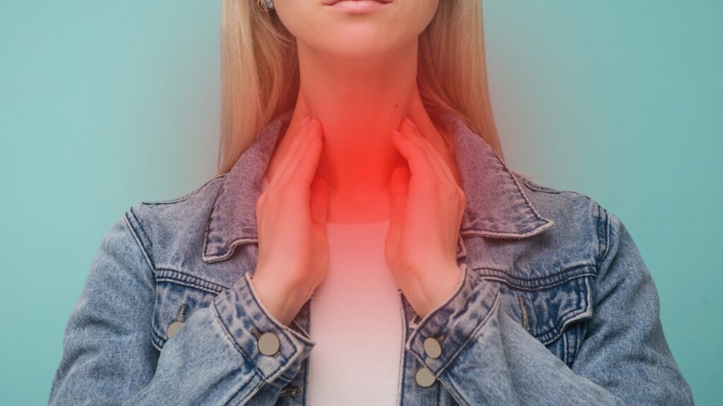 Femme se tenant au niveau de la gorge qui est rouge pour montrer une inflammation